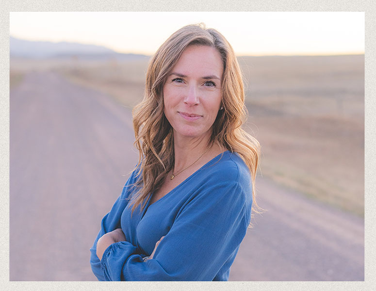 Kara M. standing on a scenic Colorado road with the Front Range mountains in the background, captured in natural light.