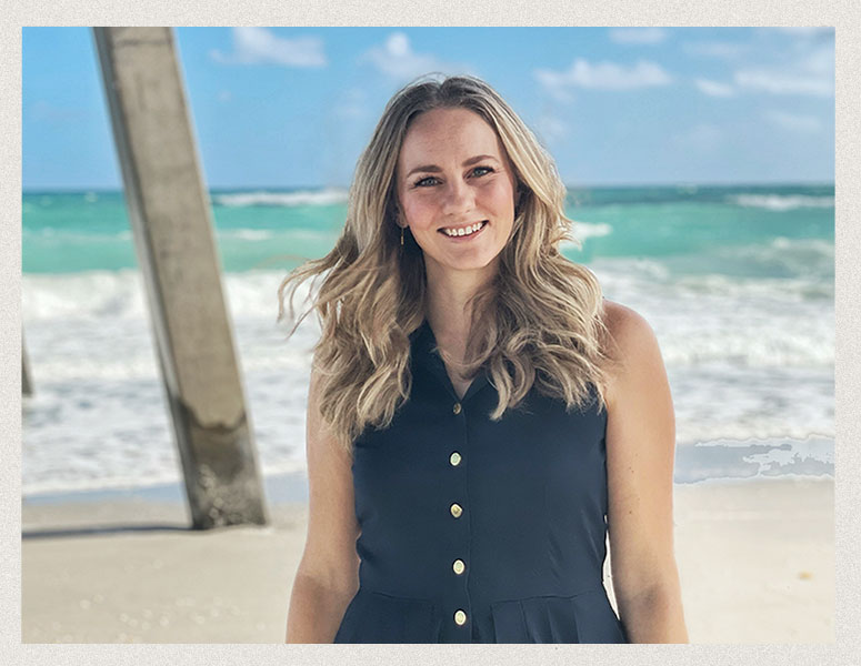 Lara M. standing on the beach outside her luxury vacation rental home, with stunning turquoise waters in the background.