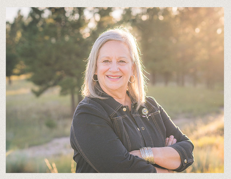 Laura Taylor wearing a green blouse, standing against a backdrop of pine trees in Douglas County, Colorado.