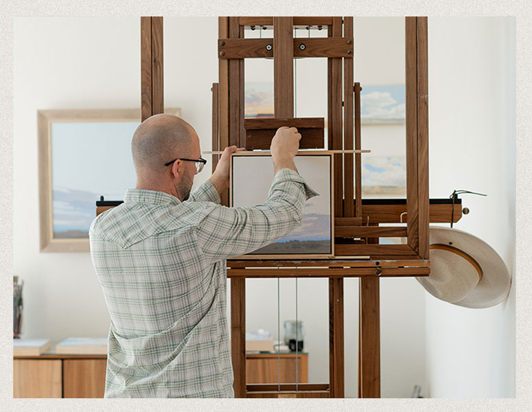 Michael Magrin setting up his oil painting in his home art studio, adjusting the canvas on his easel.