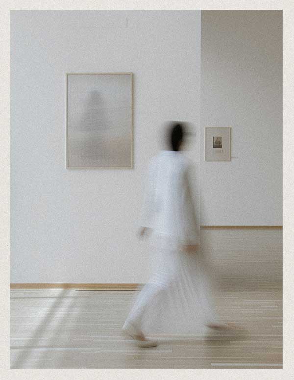 Gallery visitor browsing fine artwork in a neutral setting.