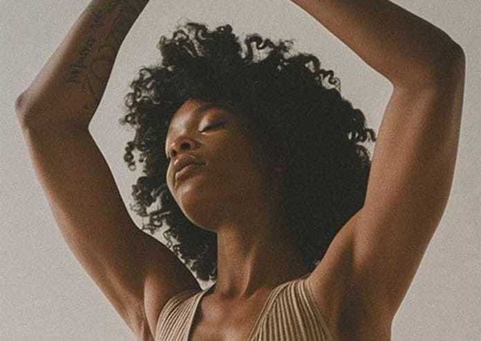 who-we-serve-wellness-studio Woman in organic tan tank top in Urdhva Hastasana yoga pose.